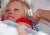 De moeder, haar nieuwe baby vasthoudend, laat haar temperatuur opmeten door middel van een oorthermometer.