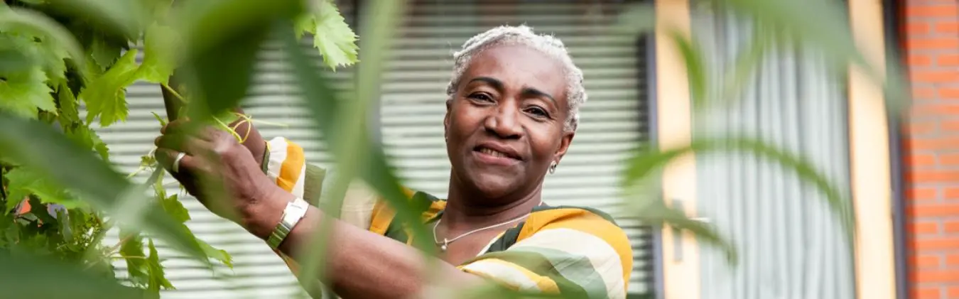 Vrouw staat in de tuin en kijkt lachend in de camera