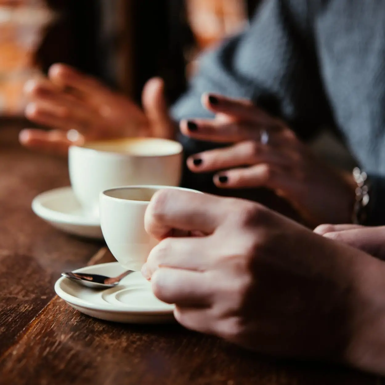 Koffiekopjes zitten op een tafel. Mensen handen zijn te zien bij de kopjes
