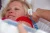 De moeder, haar nieuwe baby vasthoudend, laat haar temperatuur opmeten door middel van een oorthermometer.